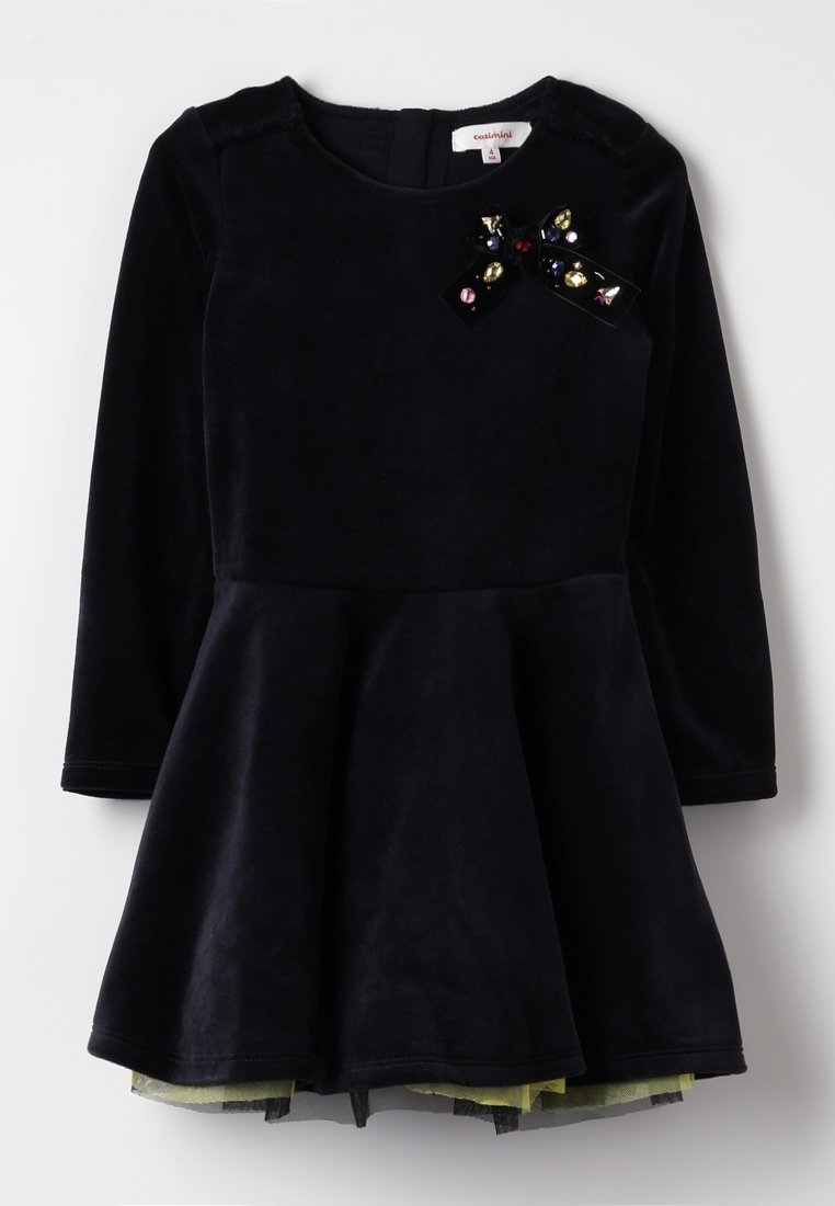 Navy velvet dress with a fitted bodice and flared skirt; features a decorative black bow with multicolored gems on the front. Long sleeves.