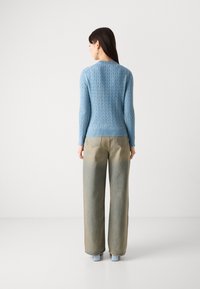 Light blue cable-knit sweater with a ribbed hem, paired with light-wash wide-leg jeans and blue block-heeled shoes.