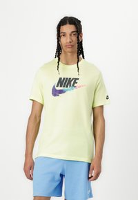 Svijetložuta pamučna majica s velikim višebojnim Nike logom. Uparen s svijetloplavim kratkim hlačama, koje prikazuju opušteni dizajn.