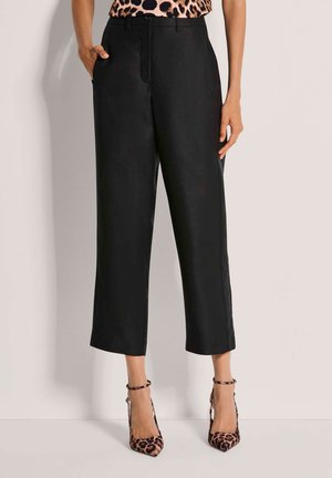 Schwarze, weit geschnittene Hose aus glattem Material, mit seitlichen Taschen und hoher Taille. Komplettiert mit Leopardenmuster-Pumps.