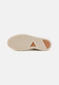 Shoe sole, light beige rubber with a patterned tread, features a triangular orange accent. Smooth texture with logo detail.