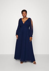 Navyblaues Maxikleid mit tiefem Ausschnitt, langen Ärmeln und tailliertem Bund. Hergestellt aus fließendem, leichtem Stoff mit durchsichtigen Akzenten.