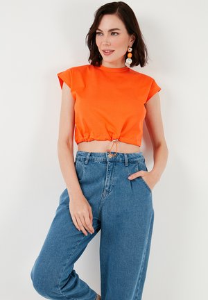 T-shirt cropped arancione con maniche corte, dotato di cordoncino in vita. Abbinato a jeans in denim blu a vita alta.