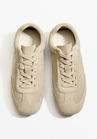 Beige mokka-tennarit, joissa on pyöreä kärki, nauhakuittaus ja sävy säilyttävä tikkaus. Pehmeä pinta ja minimalistinen siluetti.