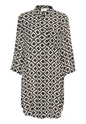Chemise à motifs noir et blanc avec des formes de diamant, manches longues, fermeture par boutons, et une poche sur le côté gauche de la poitrine. Texture de tissu douce.