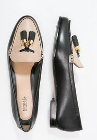 Mocassins en cuir noir avec un panneau en cuir beige, ornés de pampilles et d'accents dorés. Talon plat et détails cousus.
