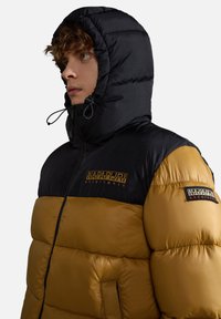 Giacca invernale imbottita nera e oro con cappuccio, dotata di lacci elastici, toppe con logo sul petto e sulla manica, e texture trapuntata.