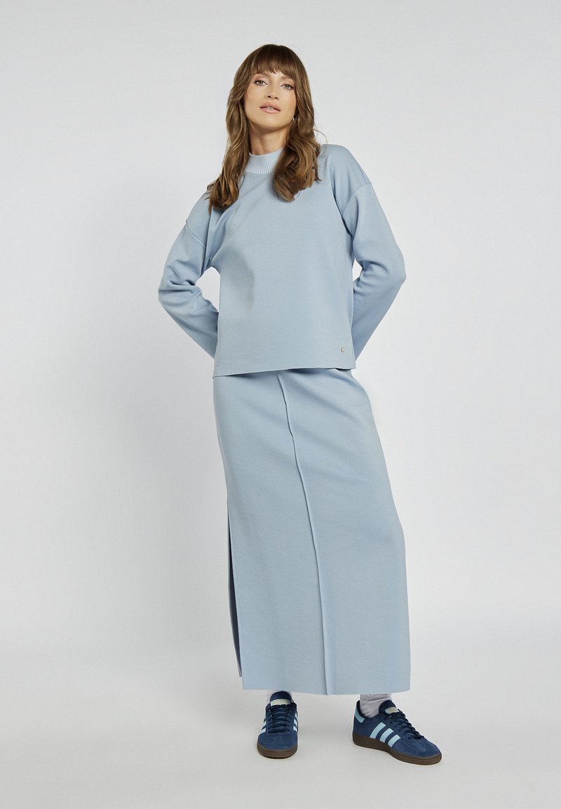 Jasnoniebieska bluza z ribbed dekoltem, dopasowana długa spódnica z bocznym rozporkiem oraz niebieskie sneakersy z białymi paskami. Gładka tekstura.