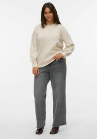 Pull en beige texturé avec des points en relief, coupe décontractée et manches longues, associé à un jean gris taille haute et jambe droite, et des bottes foncées.