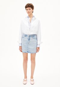 Chemise blanche à boutons, sous-col bleue claire, jupe en denim courte en délavé léger, longueur aux genoux, associée à des chaussures rose pâle. Texture lisse et plate.