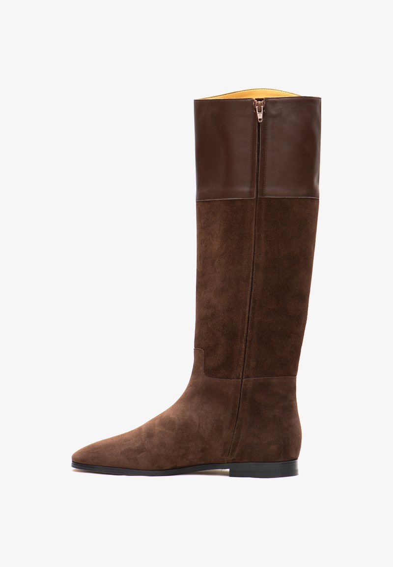 Stivale in suede marrone alto fino al ginocchio con parte superiore in pelle liscia, zip laterale, punta affilata e suola piatta in gomma. All'interno presenta foderatura gialla.