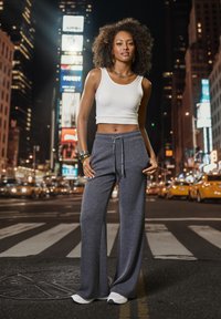 White crop top with a round neckline, paired with dark gray wide-leg pants featuring a drawstring. Worn with white sneakers. Nighttime city backdrop.