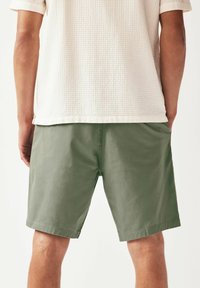 Shorts vert olive en tissu doux, coupés droit et arrivant au-dessus du genou, avec des poches latérales et un ourlet cousu.