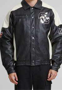 Veste en cuir noire et crème avec fermeture à pression à l'avant, taille côtelée et accents graphiques sur les manches et la poitrine. Comprend une poche zippée.