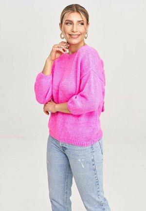 Helles pink gestricktes Sweatshirt mit lockerer Passform, Rundhalsausschnitt und 3/4-Ärmeln. Kombiniert mit hellblauen, verwaschenen Jeans.
