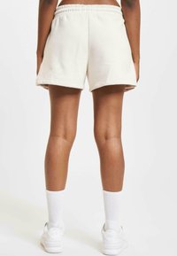 Cream-colored cotton shorts with a relaxed fit, featuring an elastic waistband and turned-up hems. Worn with white ankle socks and sneakers.