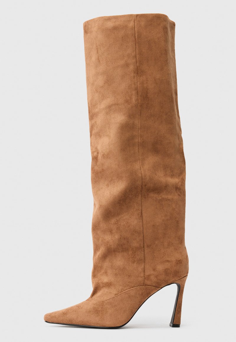 Korkeat ruskeat mokkasaappaat, joissa on terävä kärki ja kapea stiletto-korko, tasaisella vaaleanharmaalla taustalla.