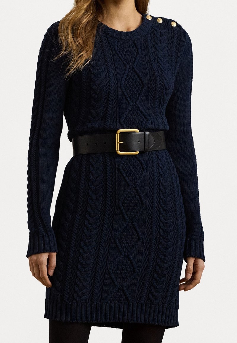 Robe-pull en maille bleu marine avec motifs torsadés, poignets et ourlet côtelés, ornée de boutons dorés sur l'épaule et d'une ceinture noire.
