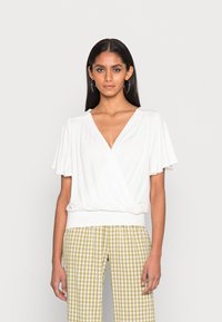 Weißes, kurzärmliges Oberteil mit V-Ausschnitt und gerafftem Detail an der Taille, kombiniert mit grün-weiß karierten Hosen. Angenehme Textur.