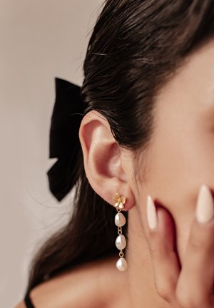 Goldene blumenförmige Ohrringe mit drei hängenden Tropfenperlen. Das Design verfügt über eine zarte Kette und eine glatte, glänzende Textur.