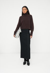 Jersey recortado burdeos, falda maxi negra texturizada y bolso de mano plateado con estampado de serpiente. Unos zapatos negros con acentos plateados completan el conjunto.