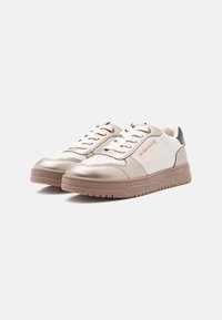 Pár béžových a bílých volnočasových tenisek se světlými hnědými podešvemi a tkaničkami, s logem značky na boku, nafocených na bílém pozadí.