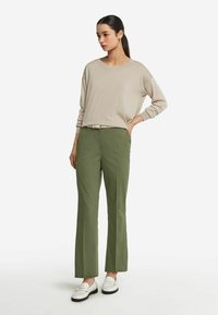 Beige långärmad tröja tillsammans med olivgröna byxor. Byxorna har rak skärning; skorna är vita loafers med svarta sulor.