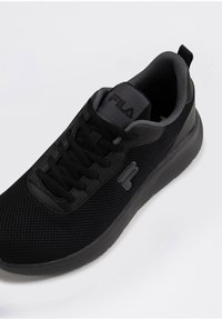 Svart atletisk sneaker med mesh-övre, texturerad gummisula, snörning och Fila-logotyp på tungan och sidan. Har en vadderad krage.