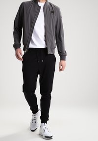 Gray bomber jacket with black accents, zip front, and ribbed cuffs paired with black joggers and white sneakers. Casual athletic look.