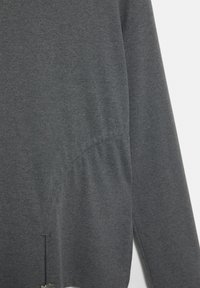 Siva dolgotrajna majica z dolgimi rokavi iz mehke, teksturirane tkanine. Ima nabrano podrobnost na strani, rob s razporkom in subtilno všitje.