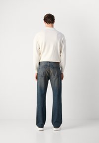 Suéter blanco de manga larga, combinado con jeans de pierna amplia azules con bolsillos traseros. Textura suave, diseño casual y color de mezclilla desgastado.