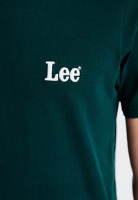 Zelené bavlněné tílko s bílou vyšívanou ikonou "Lee" na levém prsou. Krátké rukávy a design s kulatým výstřihem. Měkká textura.