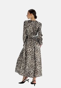 Langes Leopardenmuster Kleid in Beige und Schwarz, mit langen Ärmeln, einer taillierten Taille und einem fließenden Saum. Getragen mit schwarzen Absätzen.