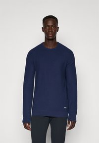 Sweater azul-marinho de gola redonda em tecido de malha suave, com mangas longas, punhos canelados e um pequeno detalhe de logótipo perto da bainha.