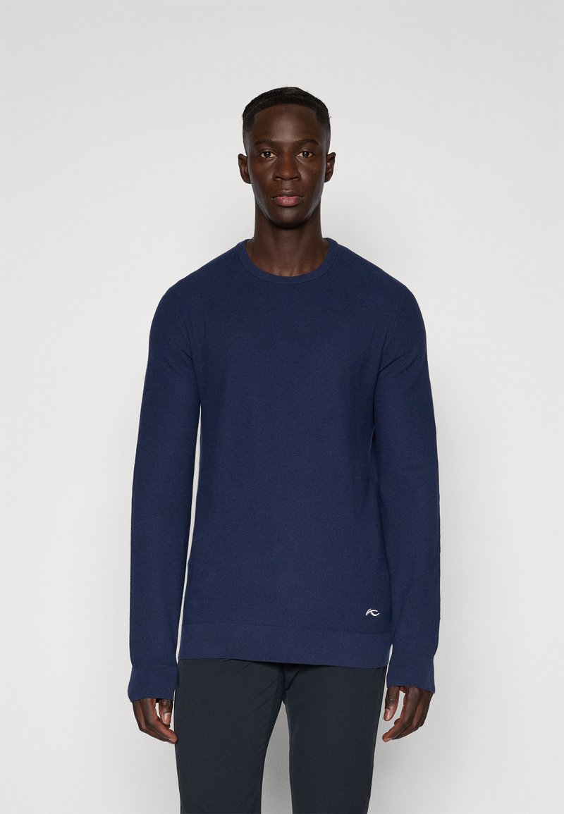 Sweater azul-marinho de gola redonda em tecido de malha suave, com mangas longas, punhos canelados e um pequeno detalhe de logótipo perto da bainha.