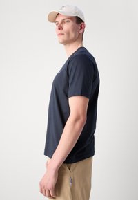 Marineblå kortærmet T-shirt med rund halsudskæring. Letvægtsstof med lille logo på brystet. Modellen har lyse bukser på.