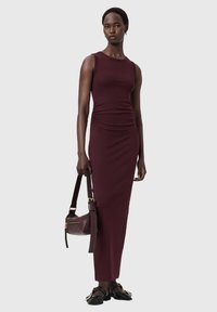 Viininpunainen hihaton mekko, jossa on ryppyinen yksityiskohta ja joustavaa kangasta. Malli kantaa samaan sävyyn sopivaa nahkalaukkua ja mustia sandaaleja.