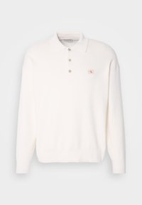 Λευκό μακρυμάνικο πόλο πουλόβερ από μαλακό ύφασμα, με κλασικό γιακά, τρία κουμπιά και μια μικρή ετικέτα λογότυπου στο στήθος.