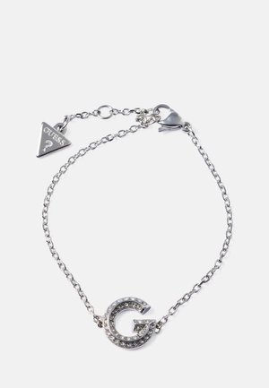 Silver chain bracelet featuring a large, glitzy "G" logo adorned with clear rhinestones and a triangular "GUESS" charm.