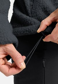 Strukturierte dunkelgraue Fleecejacke mit Reißverschluss, Hände passen einen Kordelzug an; elastische schwarze Hose mit Reißverschlusstasche.