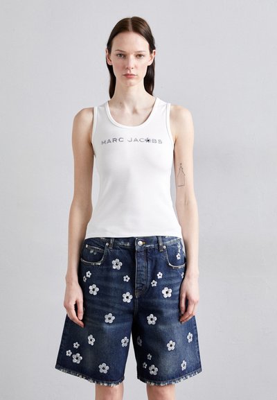 Hvid top med "Marc Jacobs" trykt i grå, parret med mørkeblå denim shorts med hvide blomstermotiver.