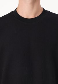 Sweatshirt negru cu model în relief, cu guler rotund și material texturat. Materialul pare moale, cu o ușoară strălucire. Fără logo-uri vizibile.