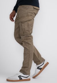 Khaki cargobroeken van een zachte stof, met meerdere zakken en een relaxte pasvorm. Gecombineerd met witte sneakers en zwarte accenten.