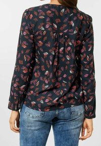 Blus med långa ärmar och svart bakgrund, prydd med ett färgglatt bladmönster i röd, rosa och vit, rynkad vid midjan och på ryggen.