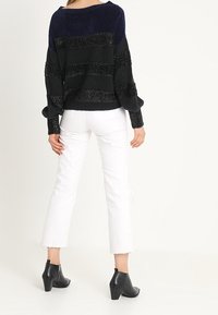 Musta- ja laivastonsiniraidallinen neulepaita, jossa rennon väljä istuvuus. Yhdistetty valkoisiin lyhennettyihin farkkuihin ja mustiin nilkkureihin, joissa on teksturoitu muotoilu.