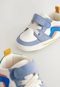 Barnens sneakers i vitt läder med blå och orange detaljer. Kardborreband, texturerad sula och en kontrasterande hälla i färg.
