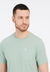 Jasnozielona koszulka z krótkim rękawem, wykonana z miękkiej bawełny. Posiada kieszonkę na piersi z metką. Okrągły dekolt i prosty materiał.