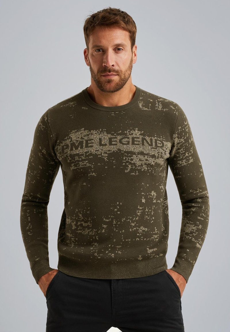 Groene gebreide trui met een textuurpatroon en de tekst "LEGEND" over de borst; ribbelboord bij de kraag en mouwen; aangesloten ontwerp.