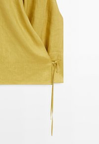 Yellow linen wrap top detail with a tie closure on the side against a white background.
