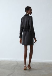 Must mustritus mustrihaga, elastse vööga ja pikkade varrukatega, sirge lõikega ja mid-thigh pikkuses. Kanda beezide kontsadega.